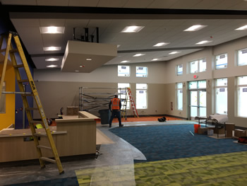 The interior of the main area of new Empire Library. Includes blue, orange, and carpet, lights overhead, and the circulation desk.