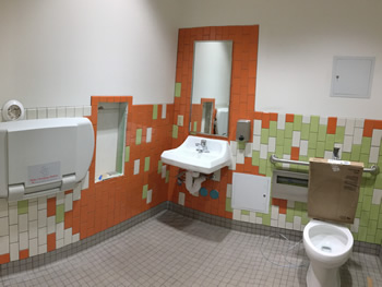 One of the restrooms in the new Empire Library. Includes orange, green, and white tiles with white walls, sink, toilet, and baby changing table.