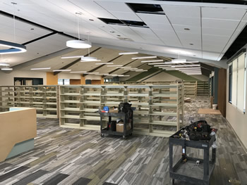 Shelving in the adult collection area with lighting overhead and gray and white carpeting.