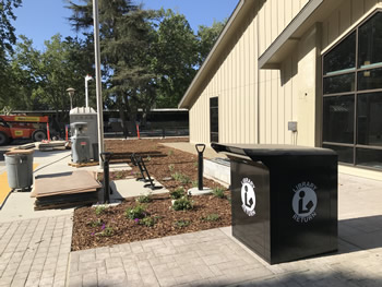 The side area of the main entrance to the Turlock Library with the black bookdrop with the words Library Return around a circle with a figure of a person reading a book. The lettering is in white.