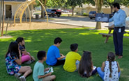 Man reading a book to a group of children in a park